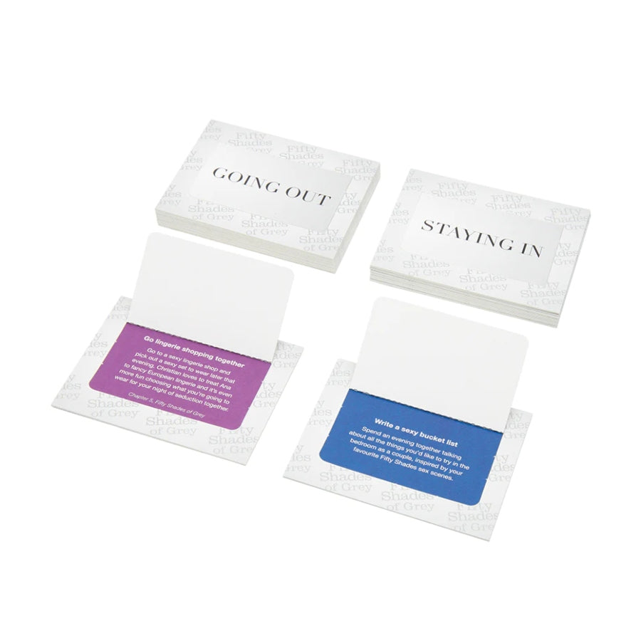 Fifty Shades of Grey Play Nice Date Night Idea Cards set featuring a box with a handle, accompanied by two open cards labeled 'Staying In' and 'Going Out', each revealing a purple or blue suggestion for romantic activities.